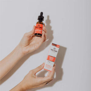 Person holding energy boost drops with CBD and CBG bottle and box in front of a white wall