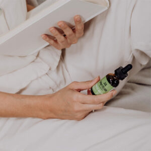 Woman in off-white blouse and pants reading a book and holding stress relief drops bottle